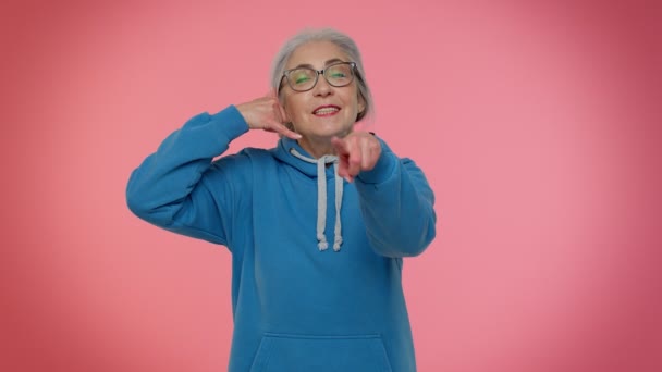 Ältere Oma grauhaarige Frau, die in die Kamera schaut und Handygesten macht wie: "Hallo, du rufst mich zurück" - Filmmaterial, Video