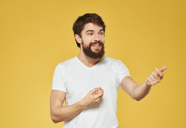 Un uomo con una barba folta su uno sfondo giallo gesti con le mani - Foto, immagini
