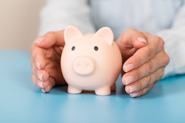Piggy banka v rukou na modrém pozadí, prostor pro text. Finance, úspory peněz - Fotografie, Obrázek