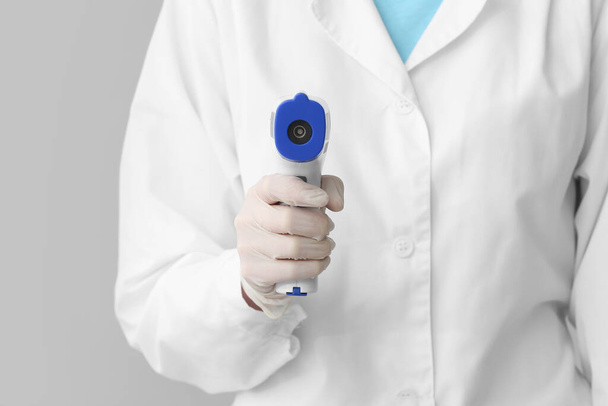 Doctor with infrared thermometer on grey background, closeup - Photo, Image