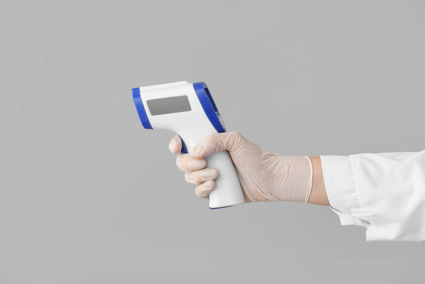 Main du médecin avec thermomètre infrarouge sur fond gris - Photo, image