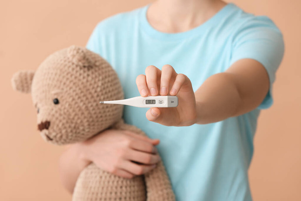 Woman with electronic thermometer and teddy bear on color background, closeup - Photo, Image