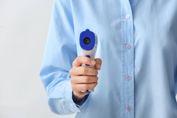 Woman with infrared thermometer on light background, closeup - Photo, Image