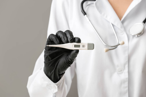 Doctor with electronic thermometer on grey background, closeup - Photo, Image
