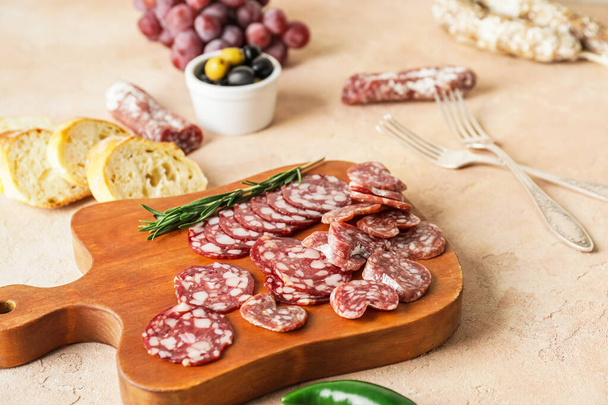 Board with tasty slices of salami on grunge background - Foto, afbeelding