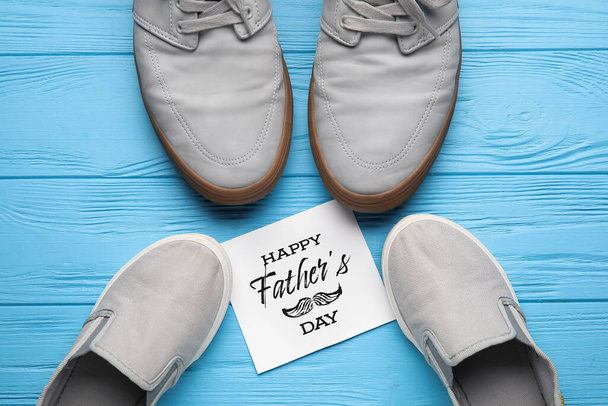 Μεγάλα και μικρά παπούτσια με ευχετήρια κάρτα για την ημέρα του πατέρα στο χρώμα ξύλινο φόντο - Φωτογραφία, εικόνα