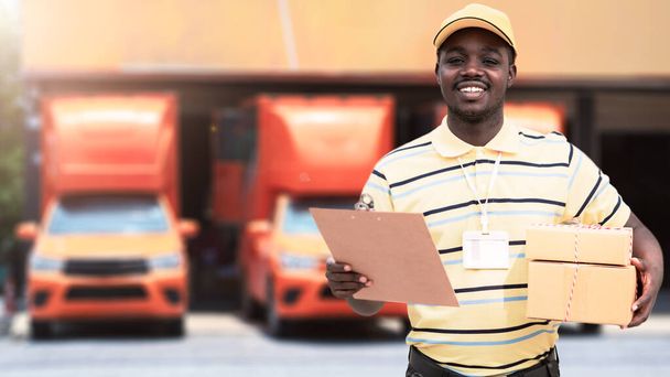 African male postal delivery courier man holding delivering package boxs in front of car - Foto, afbeelding