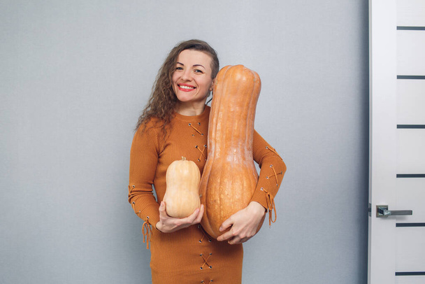 cheerful girl holding large and small pumpkin on gray background - Photo, Image