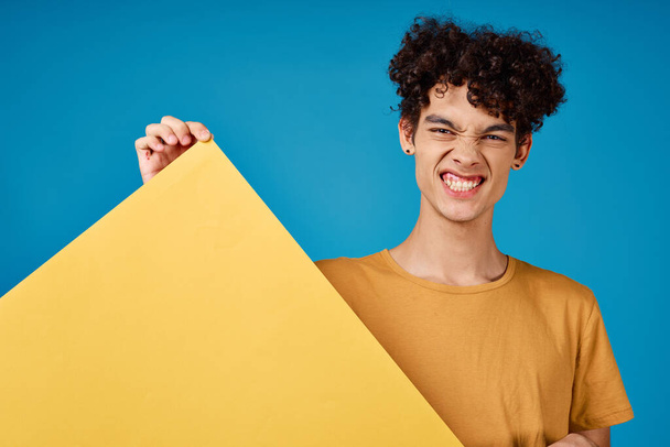 Cheerful guy with curly hair with banner in his hands in  studio on  blue background. High quality photo - Foto, afbeelding
