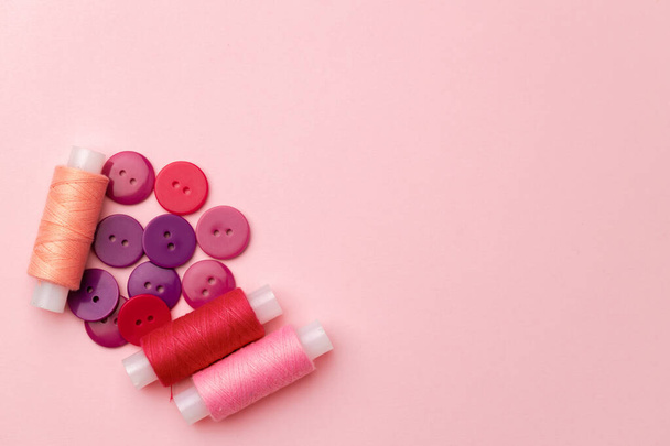 Bobines de fil multicolores et boutons sur fond rose - Photo, image