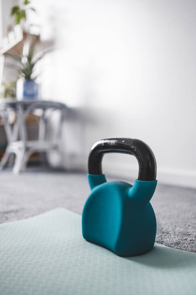 home gym with mixed fitness items including yoga mat and kettlebell with plants and decoration in the background shot at shallow depth of field with subtle grey and blue tones  - Фото, изображение