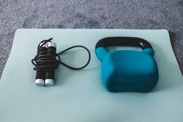 kettlebell and skipping rope on yoga mat indoor, concept of home gym and weight training vs cardio fitness styled with subtle grey and blue tones  - Foto, imagen