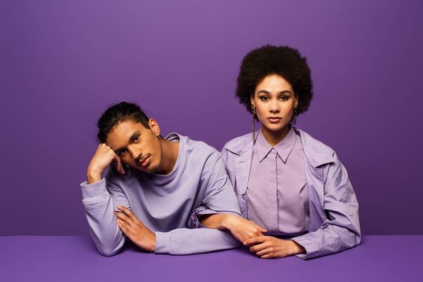 african american man and curly young woman looking at camera isolated on purple  - Fotó, kép
