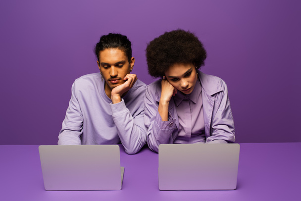 verveeld Afrikaans Amerikaans paar met behulp van laptops geïsoleerd op paars  - Foto, afbeelding