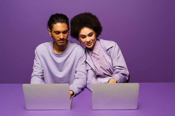 alegres freelancers afroamericanos usando computadoras portátiles aisladas en púrpura  - Foto, Imagen