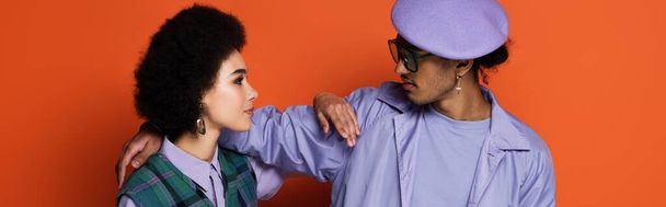 trendy african american man in beret and woman looking at each other on orange, banner - Foto, Imagem