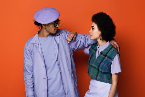 trendy african american man in beret and woman looking at each other on orange - Фото, изображение