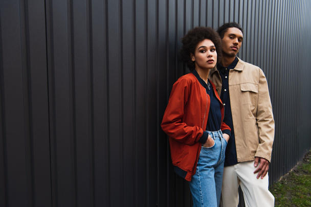 african american man looking at camera while posing with curly woman in jeans outside - Valokuva, kuva