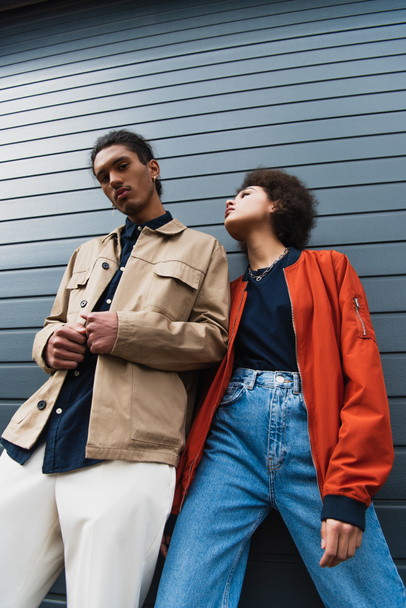 Low-Winkelansicht junger afrikanisch-amerikanischer Mann posiert mit stilvoller Frau in Jeans draußen  - Foto, Bild