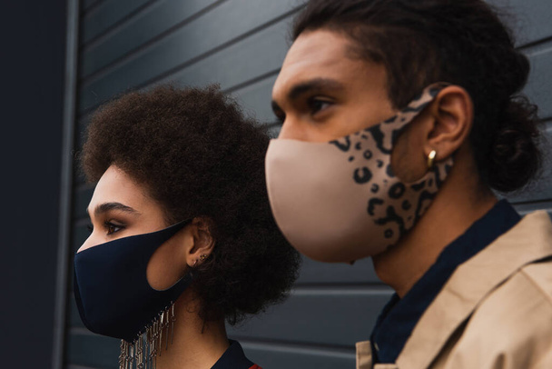 jong Afrikaans amerikaans vrouw en wazig man in stijlvolle beschermende maskers poseren buiten  - Foto, afbeelding
