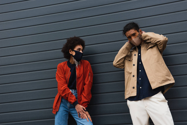 pareja afroamericana joven de moda en máscaras protectoras posando afuera - Foto, imagen