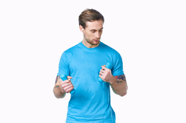 man with dumbbells in a blue t-shirt on a light background - Foto, imagen