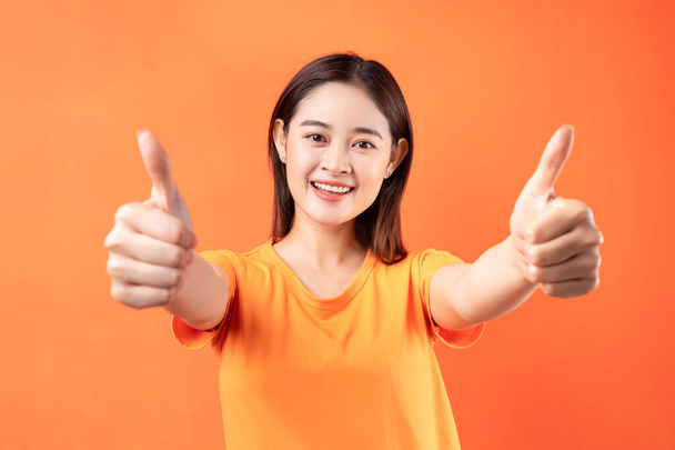 Зображення молодої азіатської жінки з помаранчевою футболкою на помаранчевому тлі - Фото, зображення