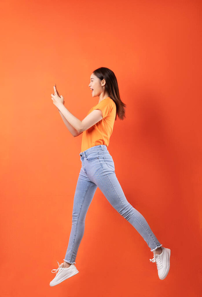 Молода азіатка в помаранчевій футболці стрибає на помаранчевому фоні - Фото, зображення