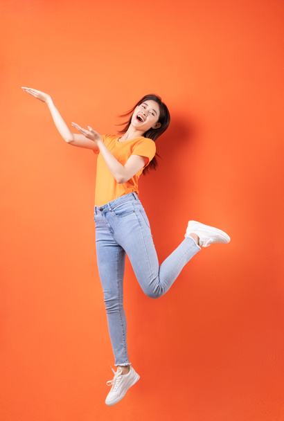 Young Asian woman wearing orange T-shirt jumping on orange background - Foto, Imagem