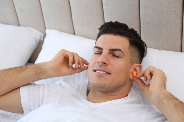 Man inserting foam ear plugs in bed - Valokuva, kuva