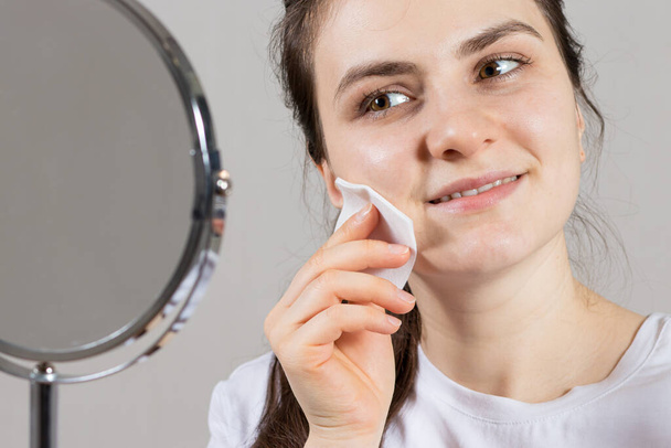 Egy 25 éves nő arc- és nyaki tonikot és vattapamacsot tart. Ránctalanító bőrápolás, vitaminok és savak az arcon - Fotó, kép