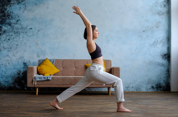 Woman in her living room in warrior yoga pose. - Foto, Imagen