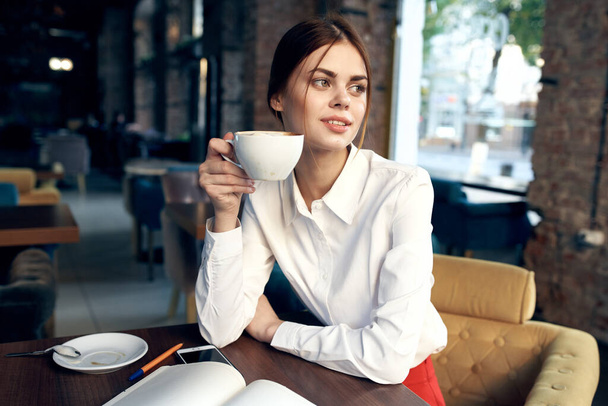 schöne Frau mit einer Tasse in der Hand sitzt an einem Tisch in einem Café  - Foto, Bild