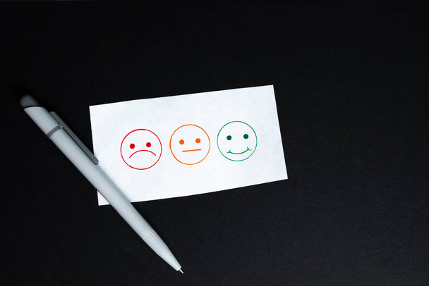 Tre faccine sorridenti da spuntare, una triste, una neutrale e una ridente, uno sfondo nero e una penna  - Foto, immagini