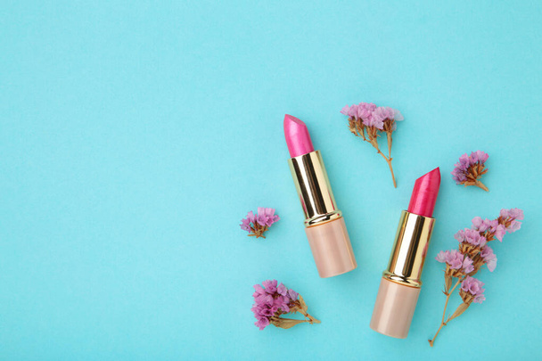 Lipstick with beautiful flowers on blue background. Top view - 写真・画像