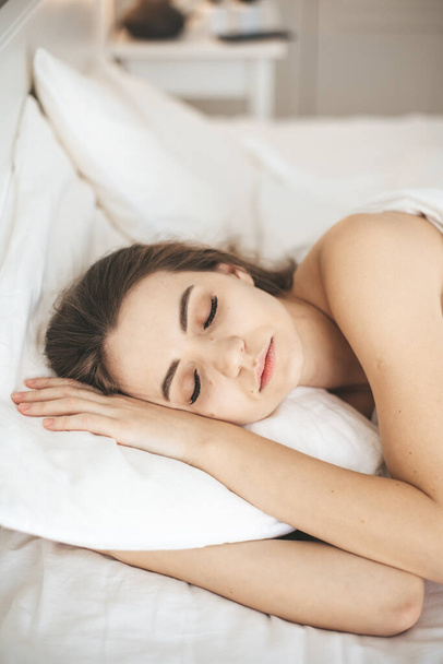 Genç bir kadın beyaz çarşaflarla yatak odasında huzur içinde uyuyor. - Fotoğraf, Görsel