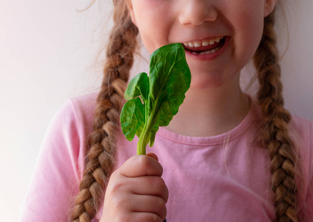 Маленькая девочка со свежим шпинатом на белом фоне. Ребенок ест натуральную сырую чистую пищу. Листовые овощи витамин Органическая вегетарианская еда супереда, питательный фруктовый салат вегетарианский здоровый образ жизни - Фото, изображение