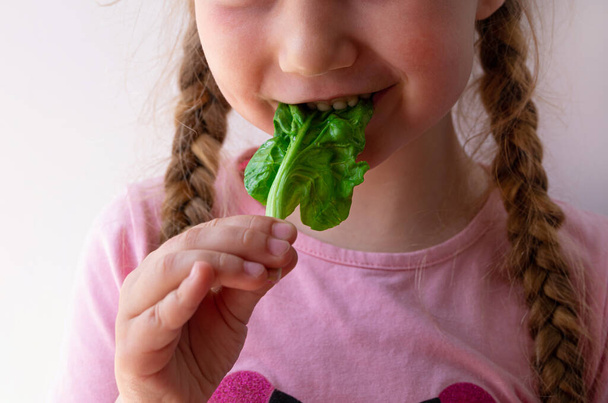 Маленькая девочка со свежим шпинатом на белом фоне. Ребенок ест натуральную сырую чистую пищу. Листовые овощи витамин Органическая вегетарианская еда супереда, питательный фруктовый салат вегетарианский здоровый образ жизни - Фото, изображение