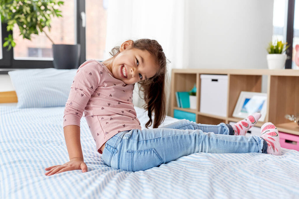 happy smiling little girl sitting on bed at home - Фото, изображение
