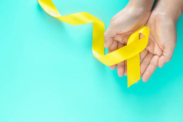 Hand holding Yellow ribbon on green background, copy space. Bone cancer Sarcoma Awareness childhood cancer cholangiocarcinoma gallbladder cancer world Suicide Prevention Day. Health concept. - Fotó, kép
