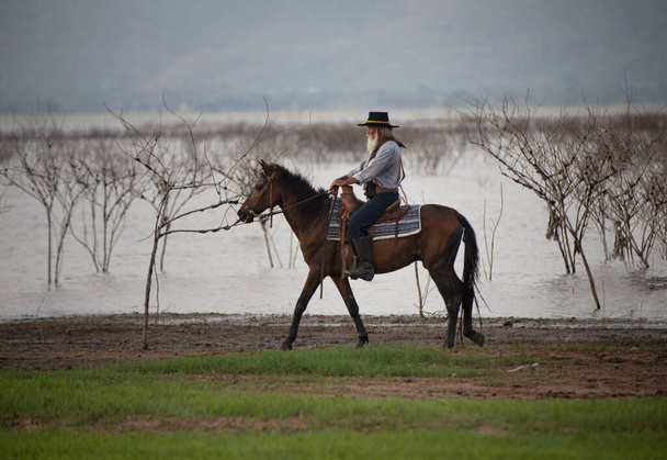 ковбой на коне против красивого заката, ковбой и лошадь на рассвете, горы, река и образ жизни с естественным освещением - Фото, изображение