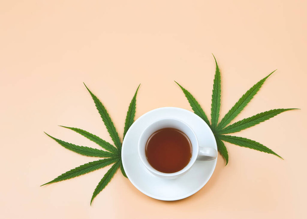 Top view or flat lay of cannabis tea and marijuana leaves on beige background. - Photo, Image