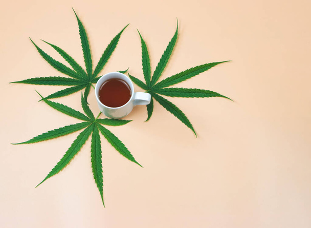 Draufsicht oder flache Lage von Cannabis-Tee und Marihuana-Blättern auf beigem Hintergrund. - Foto, Bild
