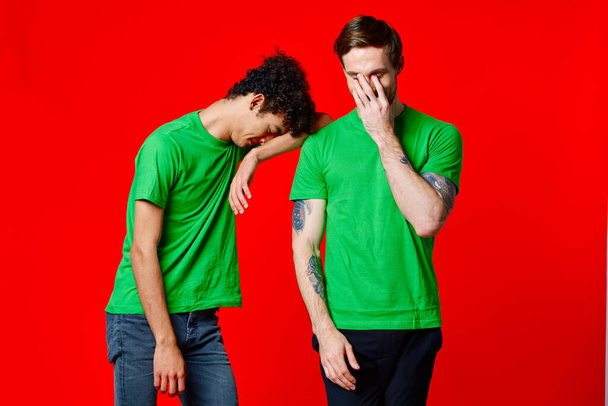 Dwóch wesołych przyjaciół w zielonych t-shirtach radość komunikacji czerwone tło - Zdjęcie, obraz