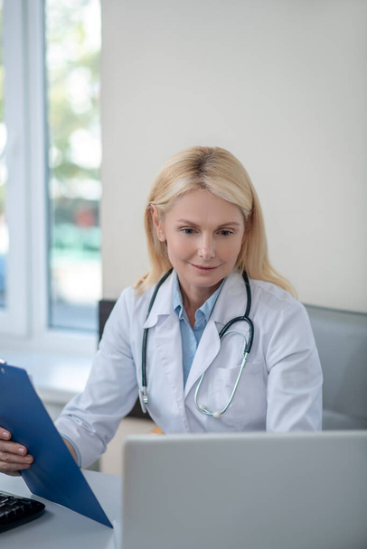 Γυναίκα γιατρός κάθεται στο γραφείο κοιτάζοντας το laptop - Φωτογραφία, εικόνα