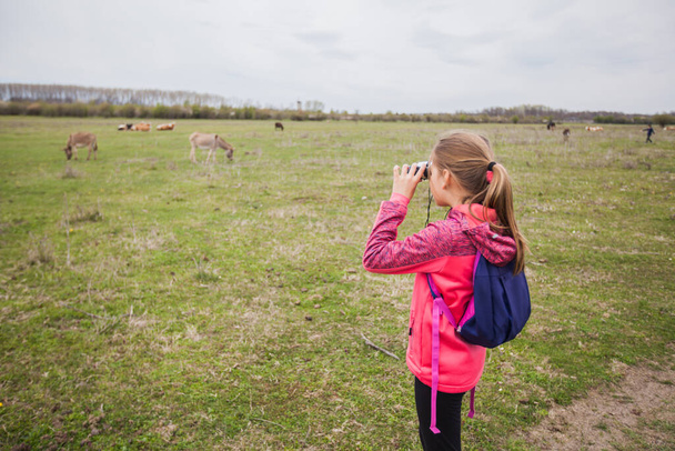 Kleines Mädchen beobachtet mit Fernglas Naturlandschaft an bewölkten Frühlingstag. - Foto, Bild