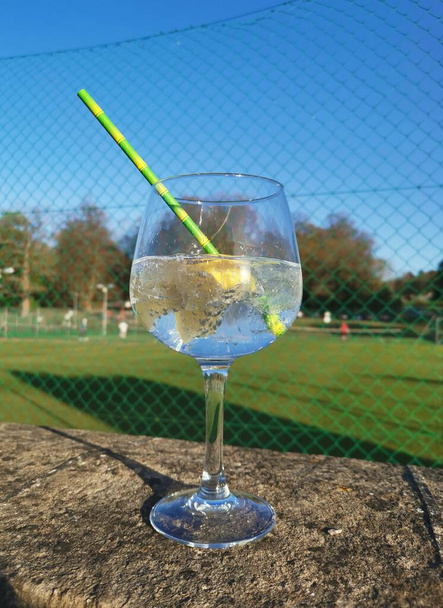 Δροσιστικό δροσερό ποτό στέκεται στον τοίχο με γήπεδα τένις πίσω - Φωτογραφία, εικόνα