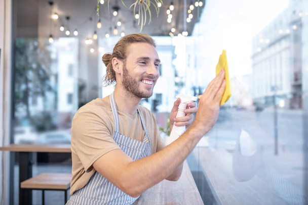 Smiling man wiping window in cafe in afternoon - Фото, зображення