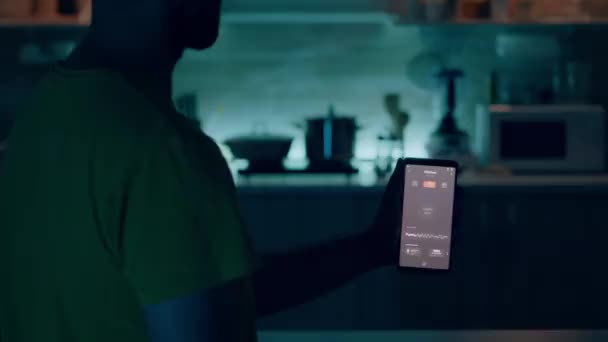 Mužské držení mobilní s ovládáním osvětlení aplikace sedí v kuchyni - Záběry, video