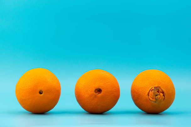 lelijke en normale sinaasappels op een blauwe achtergrond, concept van verschillende stadia van aambeien - Foto, afbeelding